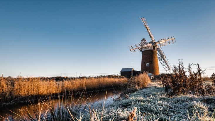 Thick frost on the ground with the windpump standing against a bright blue sky at sunrise at Horsey Windpump, Norfolk